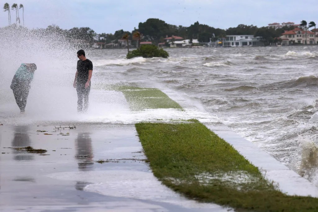 People are splashed by churning surf from Tampa Bay as Hurricane Helene passes offshore on September 26, 2024, in St. Petersburg, Florida.  Helene is forecast to become a major hurricane, bringing the potential for deadly storm surges, flooding rain, and destructive hurricane-force winds along parts of the Florida West Coast. 