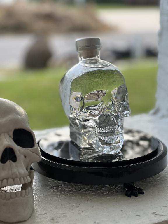 Bottle of Crystal Head Vodka on a ledge outside next to a white plastic skull, a perfect vodka for Halloween